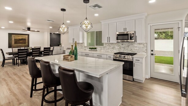 A modern kitchen with white cabinets, a large island, bar stools, a dining table, and a view of the outdoors. - Modern 4BR Home • Pool • South Scottsdale (Scottsdale)