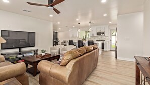 A modern living room with a leather sofa, a flat-screen TV, and a dining area with a wooden table. - Modern 4BR Home • Pool • South Scottsdale (Scottsdale)