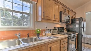 Una cucina con mobili in legno, lavello in acciaio inox, microonde, piano cottura e frigorifero.