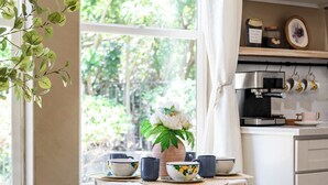 A cozy kitchen with a window, wooden stools, a table with tea cups, and a potted plant.