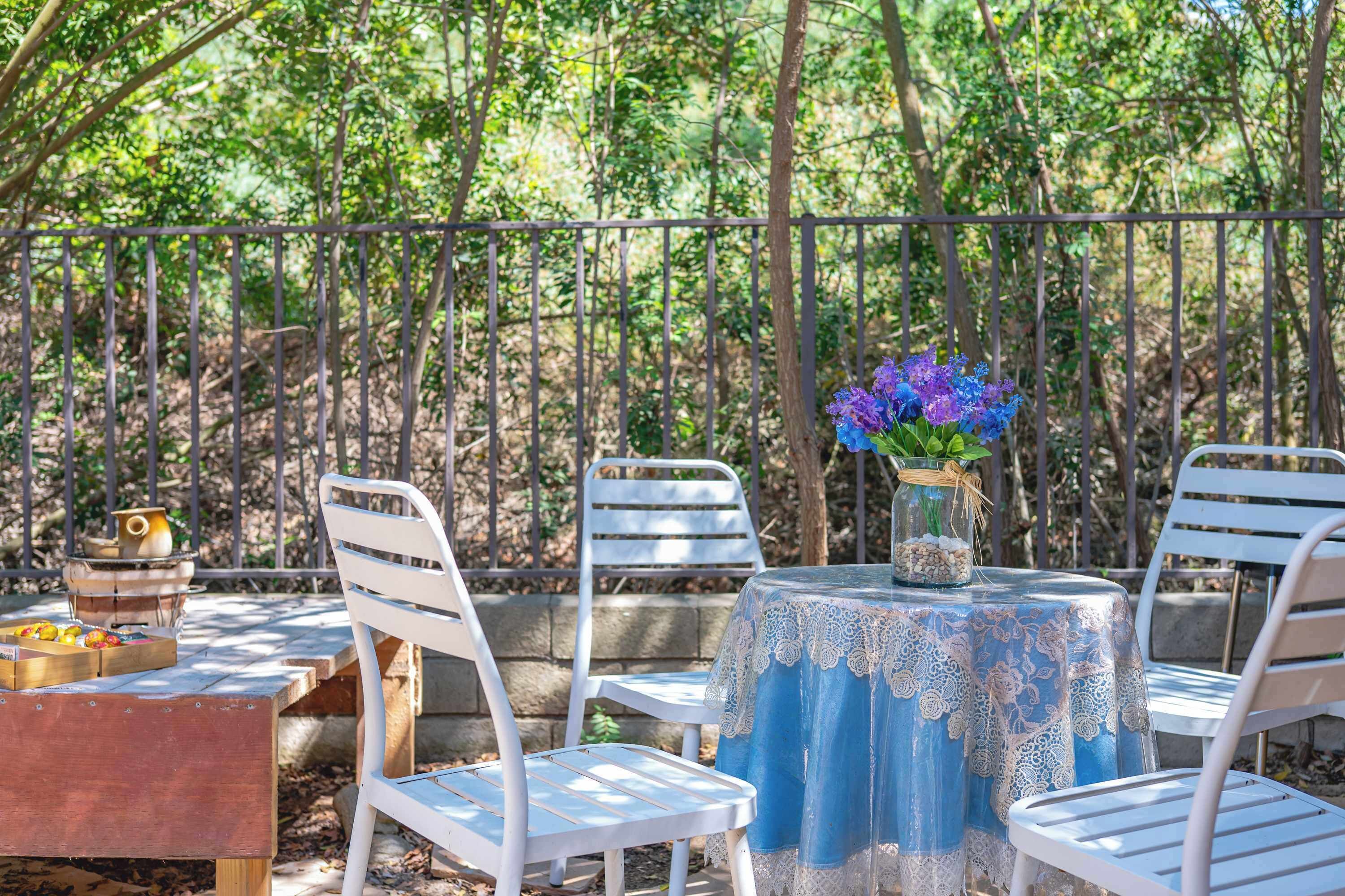 An outdoor patio with white metal chairs and a table covered with a lace tablecloth.