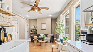 A modern kitchen with a built-in oven, a dining area with a table and chairs, a sofa, and a ceiling fan.
