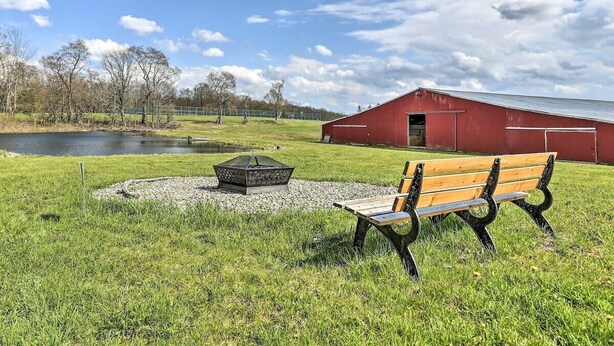 Un espace herbeux avec un banc, un foyer et une grange rouge.