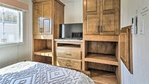 Une chambre avec des armoires en bois, un lit recouvert d’une couvre-lit à motifs et une fenêtre avec des stores.