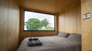 A bedroom with a large window, wooden walls, and a bed with grey bedding. - Cosy Cabin at The Coppleridge 2 (Motcombe)