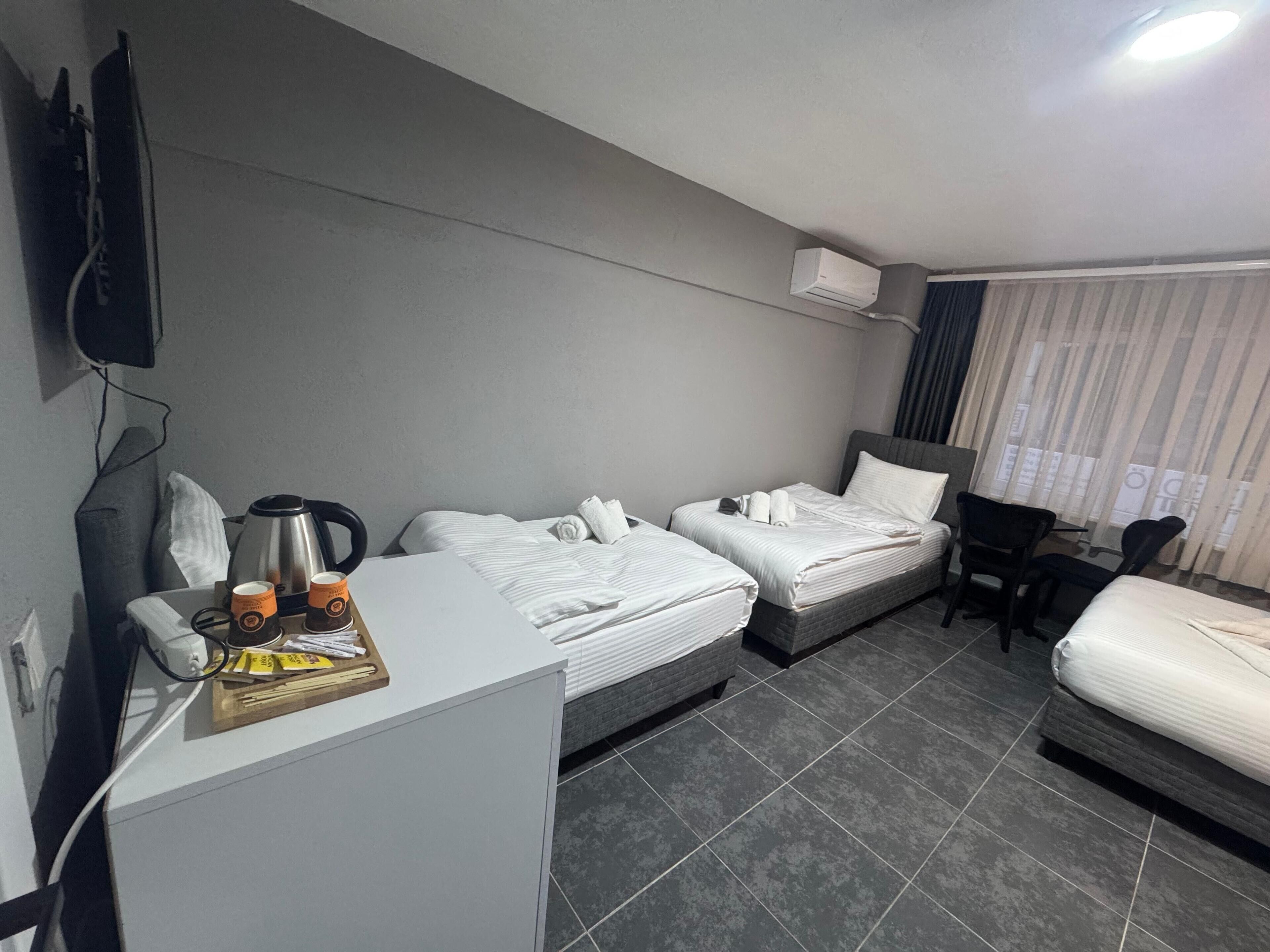 A hotel room with two beds, a desk with a coffee maker, a chair, and a TV mounted on the wall.