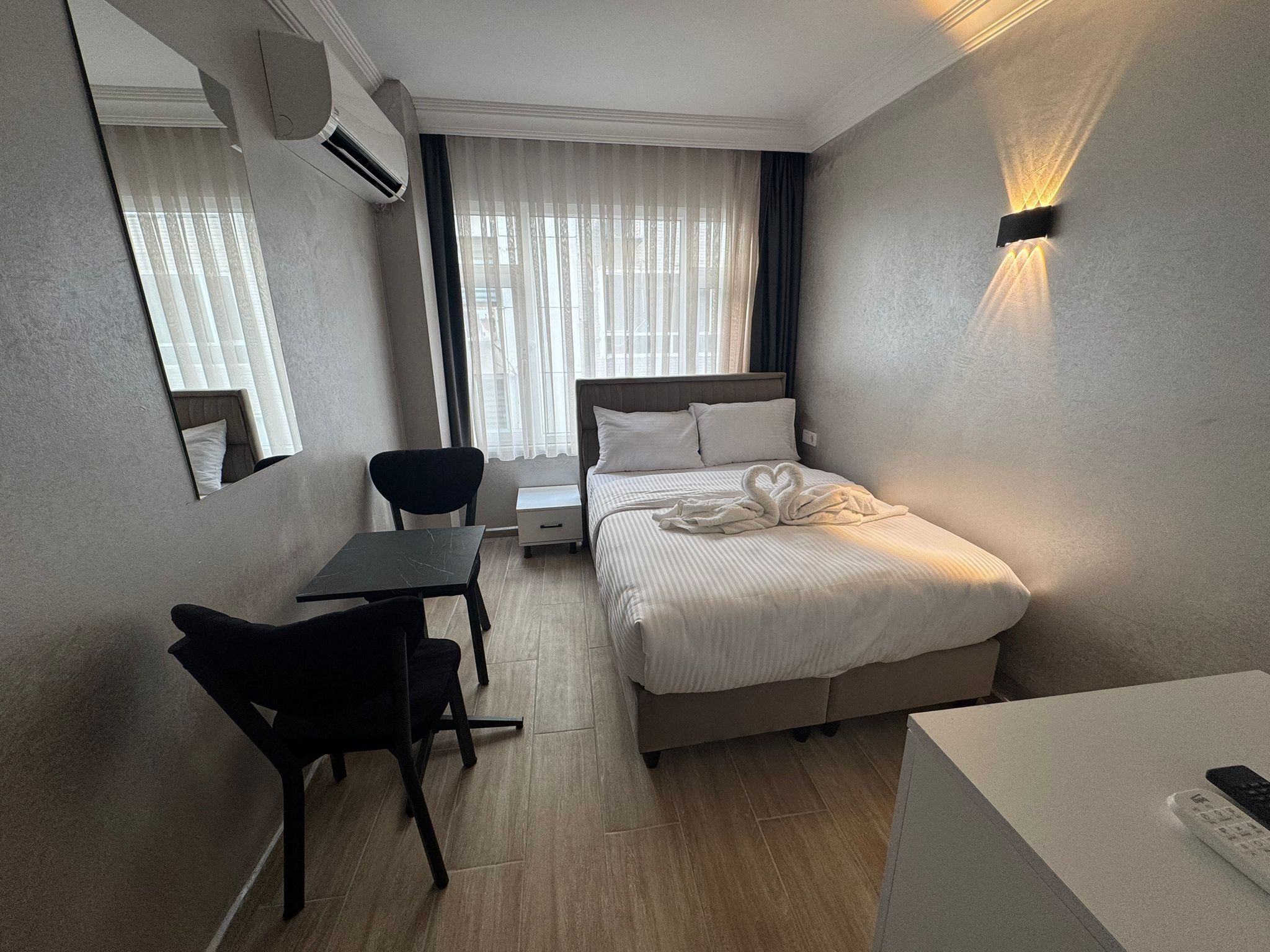 Una camera d'albergo con un letto, una scrivania, una sedia, un comodino, uno specchio e un lampadario a parete.