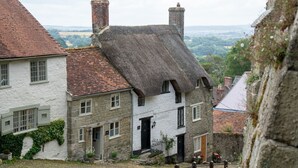 A traditional stone house with a thatched roof, white walls, and a brick chimney.