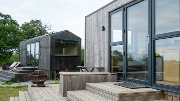 A modern wooden house with large glass windows, a deck with outdoor furniture, and a small boat.