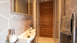 A modern bathroom with a glass-enclosed shower, a white sink with a soap dispenser, and a towel rack.