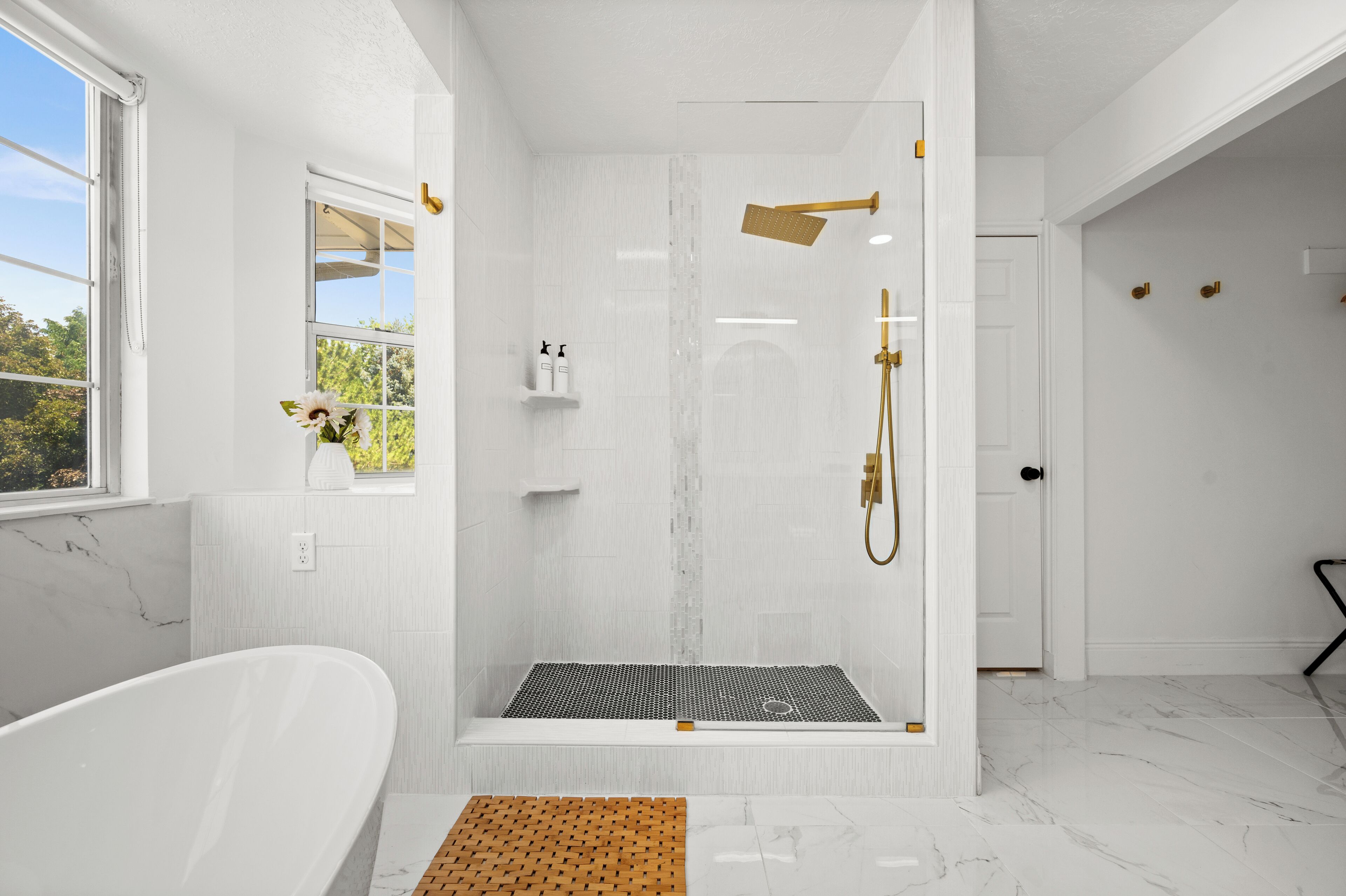 A modern bathroom with a glass-enclosed shower, a freestanding bathtub, and a small window with a view.