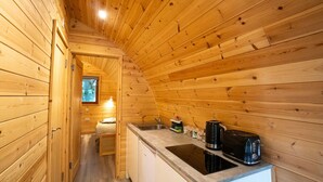 Une petite cabane en bois comprenant un coin cuisine, un petit lit et une fenêtre laissant entrer la lumière naturelle.