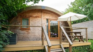 Une cabane en bois avec une porte en verre, une terrasse en bois et un parasol blanc.