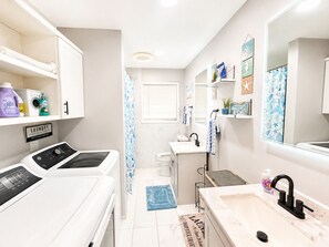 Une petite salle de bain d’hôtel équipée d’un lave-linge, d’un lavabo, d’un miroir et d’une douche.