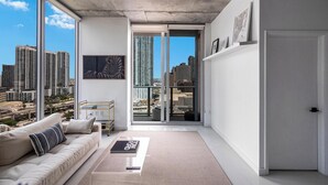 A modern living room with a large window, a sofa, a coffee table, and a door leading to a balcony with a city view. - 2bed2 bath apartment. FREE PARKING, POOL&GYM (Miami)