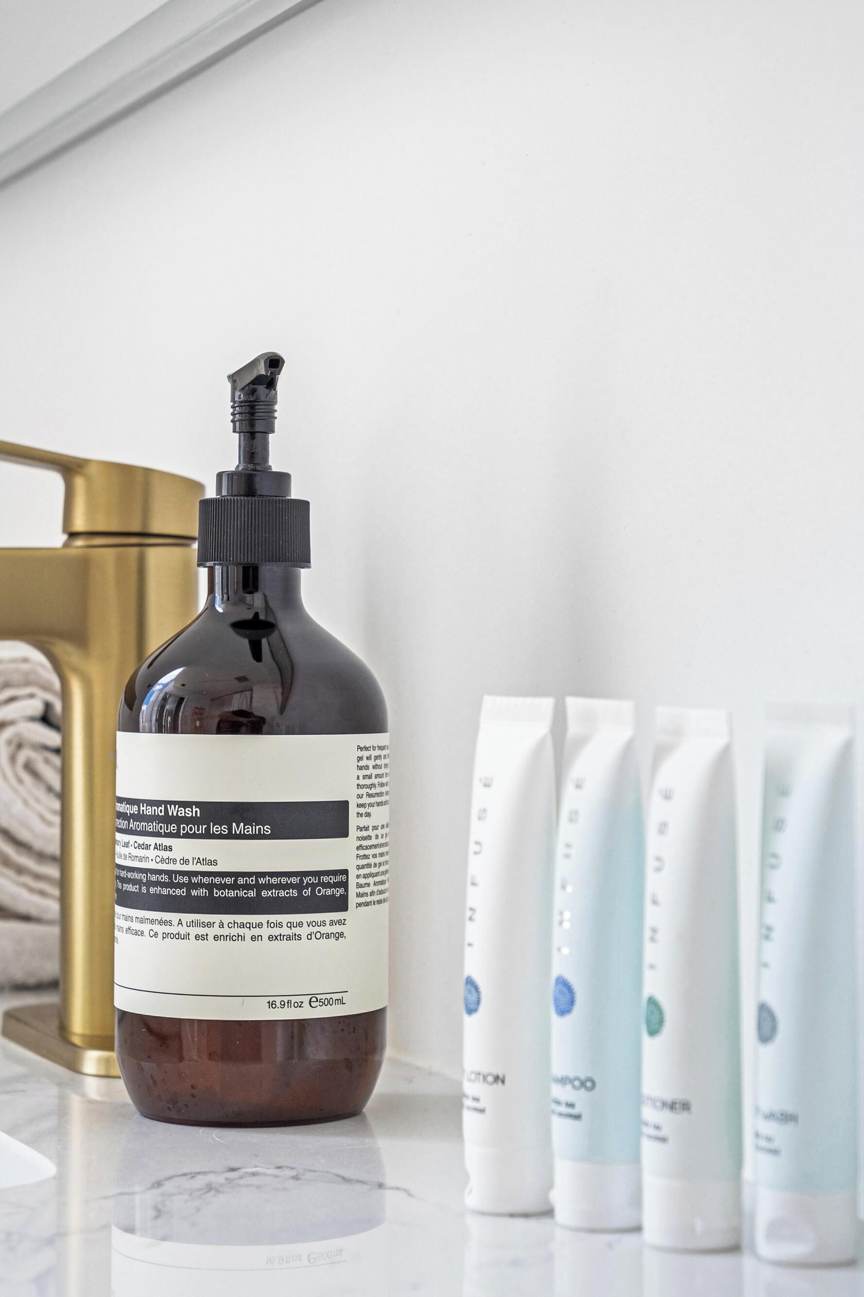 A bottle of hand wash soap and four tubes of shampoo on a marble countertop.