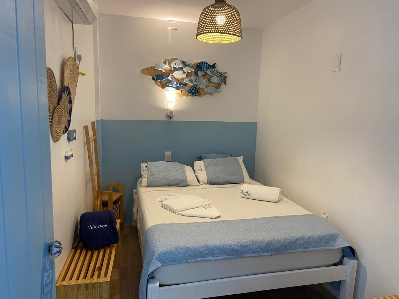 A neatly arranged bedroom with a bed, pillows, a wall-mounted light fixture, and a hanging lamp.