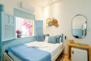 A bedroom with a bed, a window with shutters, a bedside table, a mirror, and a small refrigerator. - Pousada Vila Duju (Ipojuca)