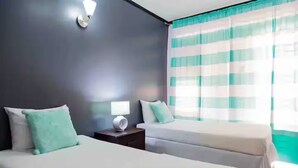Une chambre d’hôtel avec deux lits, une table de chevet avec une lampe et une fenêtre avec des rideaux à rayures.