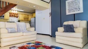 Un salon avec deux canapés de couleur crème, un tapis aux couleurs vives et une cuisine en arrière-plan.