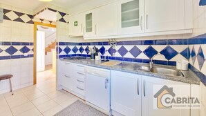 Una cocina con armarios blancos, un salpicadero de azulejos azul y blanco, una estufa a gas, un lavavajillas y un lavabo.