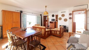 Amplia sala de estar con una mesa de comedor de madera, sillas, un sofá y una chimenea. Hay un televisor montado en la pared y un ventilador de techo.