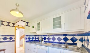 A kitchen with white cabinets, a blue and white tiled backsplash, a gas stove, a dishwasher, and a sink. - Casa da Cestaria T2 Duplex by YHA (Cabanas de Tavira)