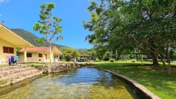 A clear pond with a house and trees in the background. - Rancho Pica Pau (Ubatuba)