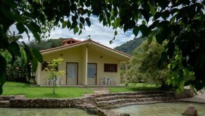 A yellow building with a red roof, surrounded by a grassy area and a small pond. - Rancho Pica Pau (Ubatuba)