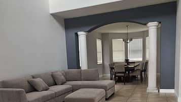 Una sala de estar amplia con un sofá modular, un reposapiés y un comedor con mesa y sillas.