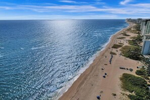A beach with a clear view of the ocean, a sandy shore, and a row of buildings along the coastline.