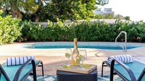 A poolside setting with a bottle of champagne, glasses, and lime wedges on a tray, surrounded by lounge chairs and a pool. - Beach Family Tiki Villa Walk to Beach Heated Pool (Pompano Beach)