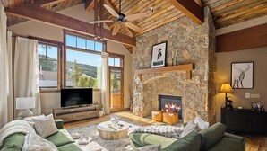 A cozy living room with a stone fireplace, green sofas, a flat-screen TV, and a ceiling fan. - Alpine 28: Luxe Keystone Mountain Home - Sleeps 16 (Dillon)