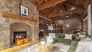 A cozy living room with a stone fireplace, wooden beams, a green sofa, and a fluffy rug. - Alpine 28: Luxe Keystone Mountain Home - Sleeps 16 (Dillon)