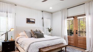 A bedroom with a bed, bedside table, lamp, and a view through a door.