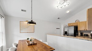 A modern kitchen with wooden cabinets, a stainless steel refrigerator, and a dining area with a wooden table and chairs.