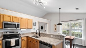 A modern kitchen with wooden cabinets, stainless steel appliances, a granite countertop, and a large window providing natural light.