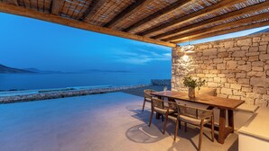 Patio esterno con muro in pietra, tavolo e sedie in legno, affacciato su un corpo d'acqua.