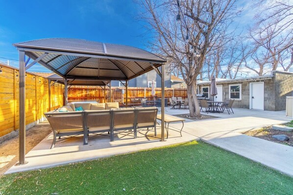 A covered patio area with outdoor furniture, a grassy lawn, and a wooden fence.