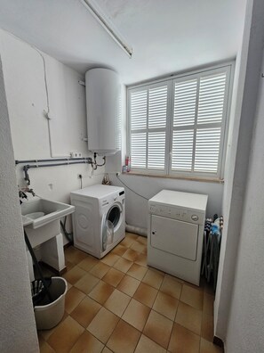 A laundry room with a washing machine, dryer, sink, and window with blinds.