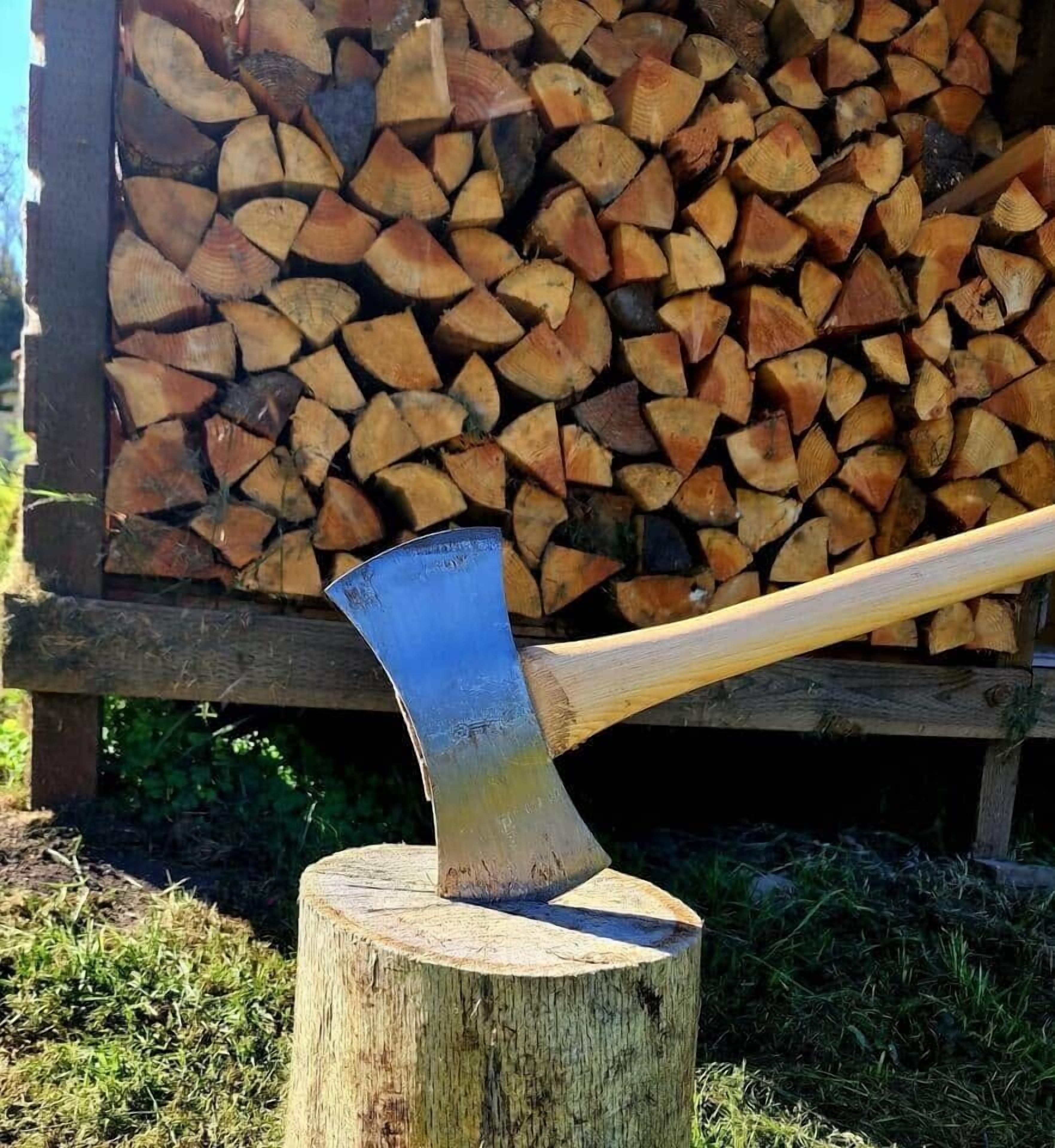 A wooden axe resting on a tree stump with a stack of firewood in the background.