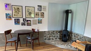 Ein gemütliches Zimmer mit Kamin aus Stein, einem runden Holztisch mit Stühlen und verschiedenen gerahmten Kunstwerken an der Wand.
