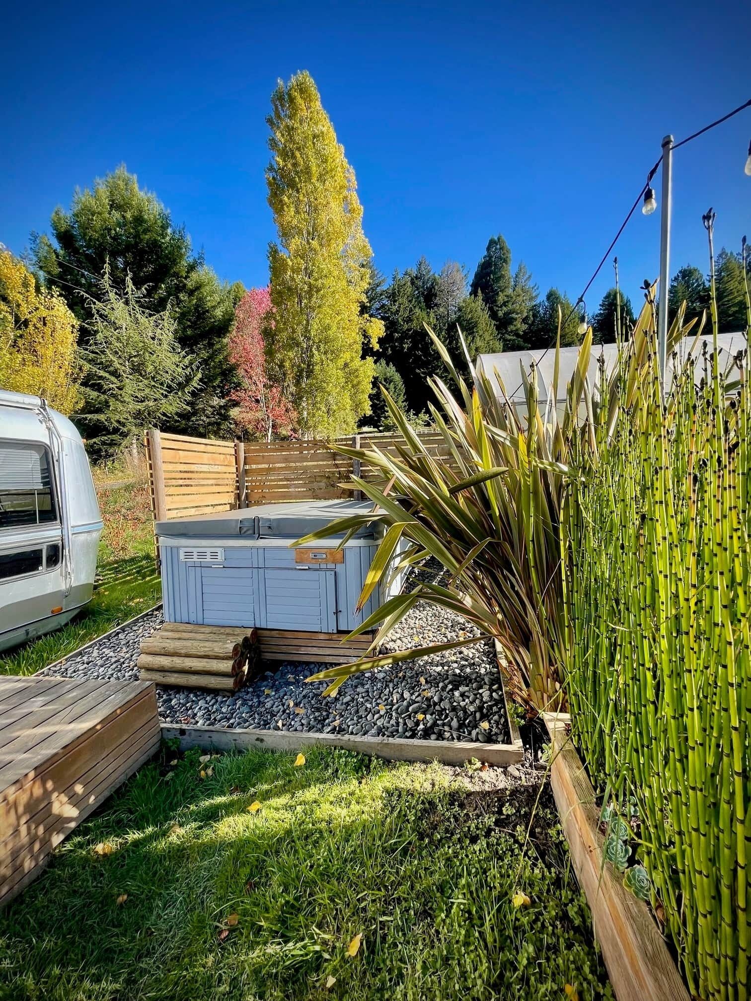 Un jardín con terraza de madera, una caravana blanca y un cobertizo azul.