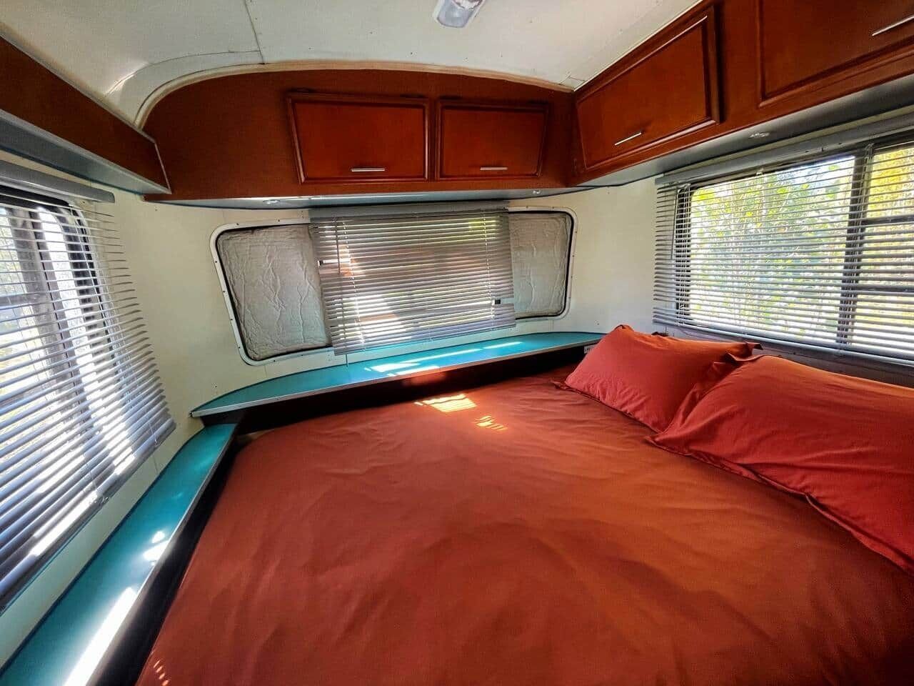 Dormitorio de una caravana compacta, con cama, armarios empotrados y ventana con persianas.