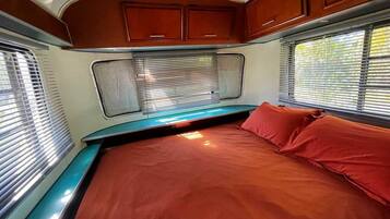 Dormitorio de una caravana compacta, con cama, armarios empotrados y ventana con persianas.