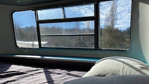 Una habitación con cama, ventana y vista a árboles y cielo.