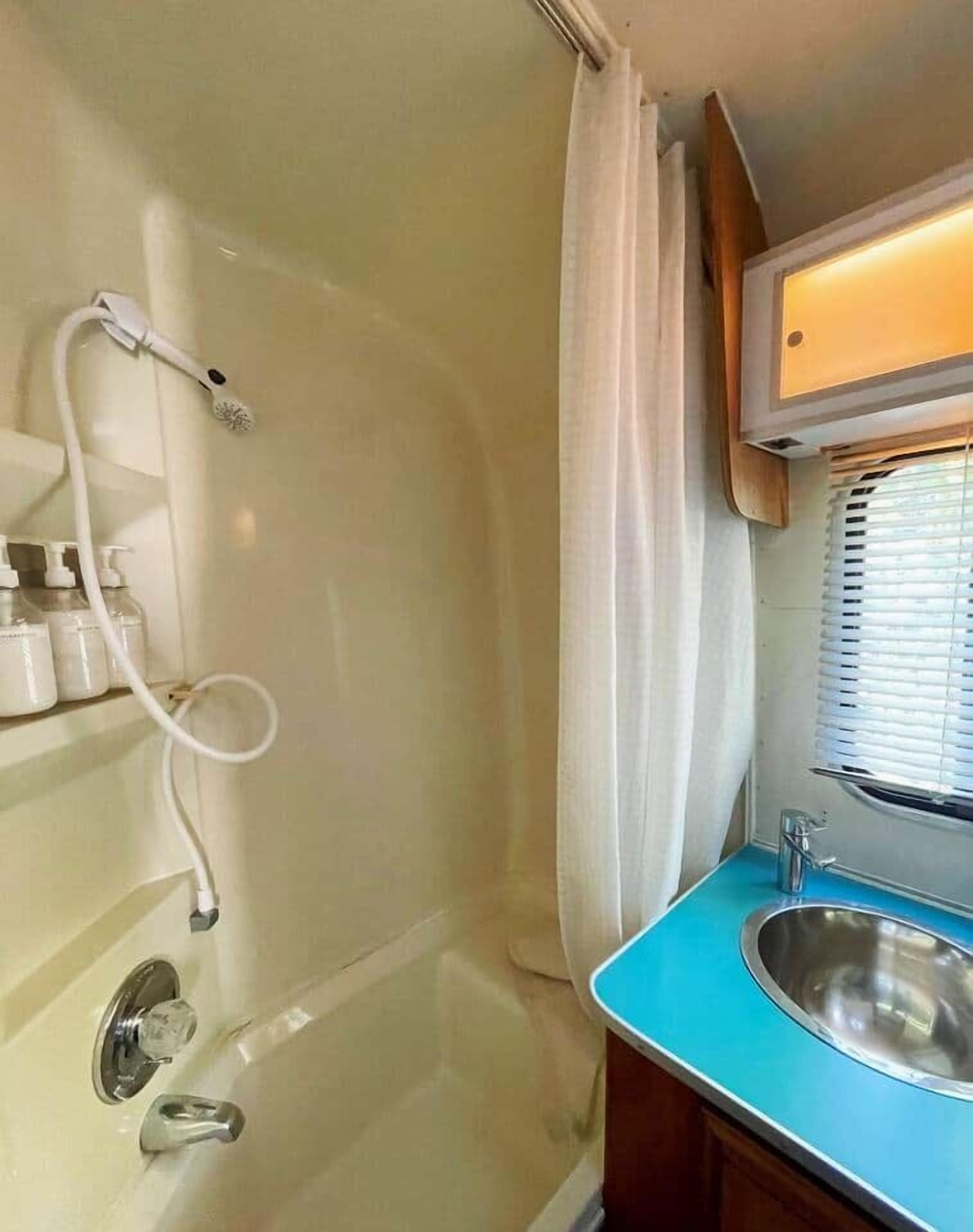Un bagno piccolo con doccia, lavandino e finestra con persiane.