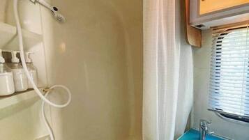 Un bagno piccolo con doccia, lavandino e finestra con persiane.