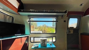 Pequeña cocina con ventana, una mesa con un libro y un televisor sobre un mueble.