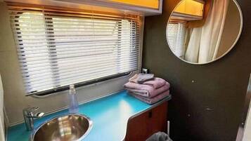 Un baño pequeño con lavamanos, inodoro y ventana con persianas.
